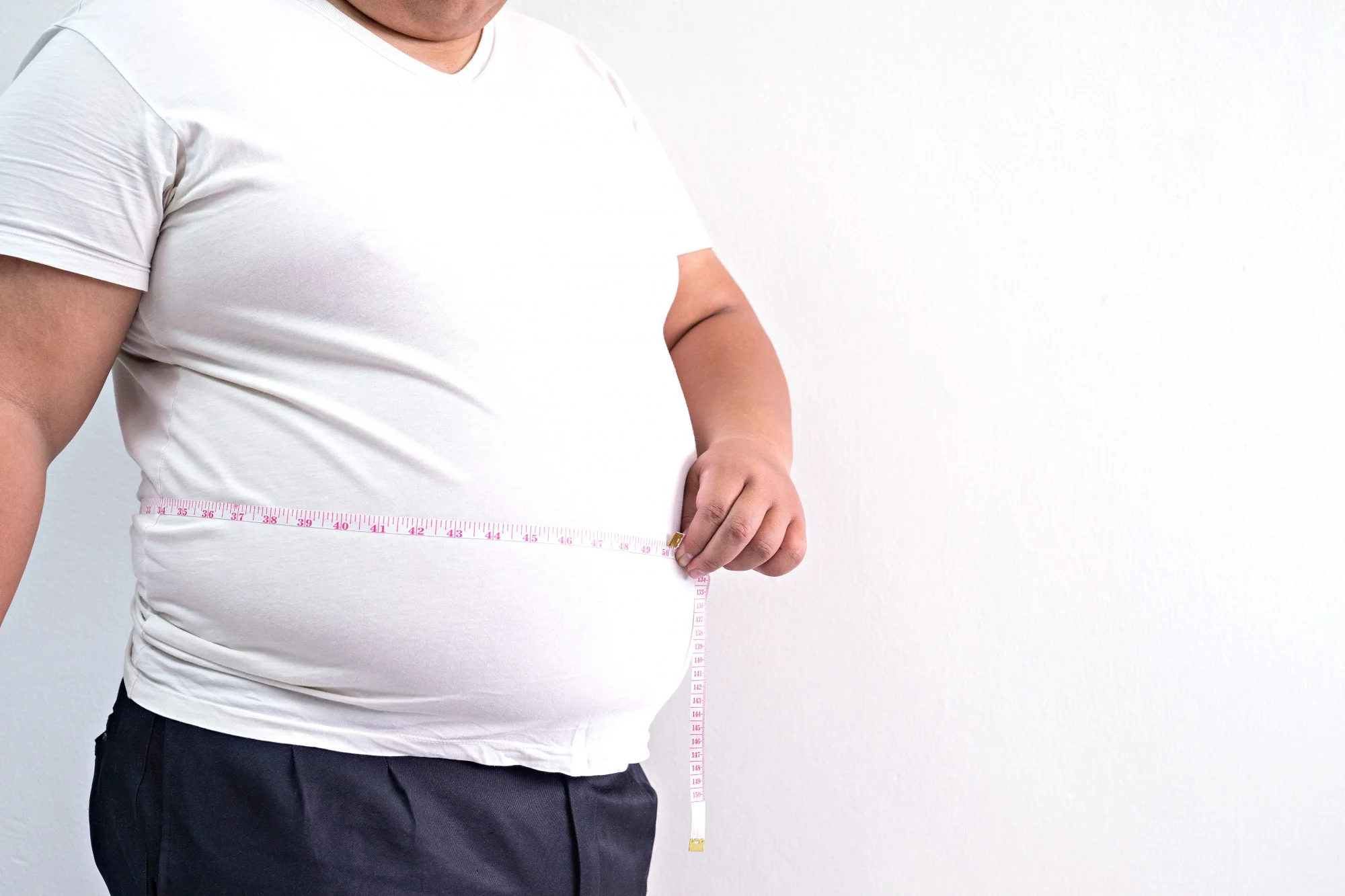 An overweight person measures their waist with a measuring tape, highlighting abdominal obesity and its connection to health risks such as metabolic disorders and sleep-related conditions.