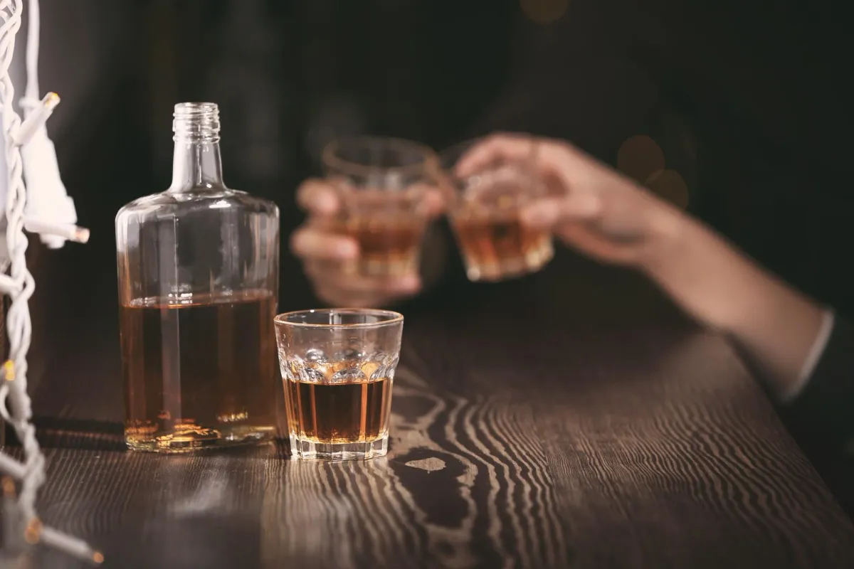 Alcohol with Minimum Calories represented by amber liquor in a glass beside a bottle during a casual cheers moment.