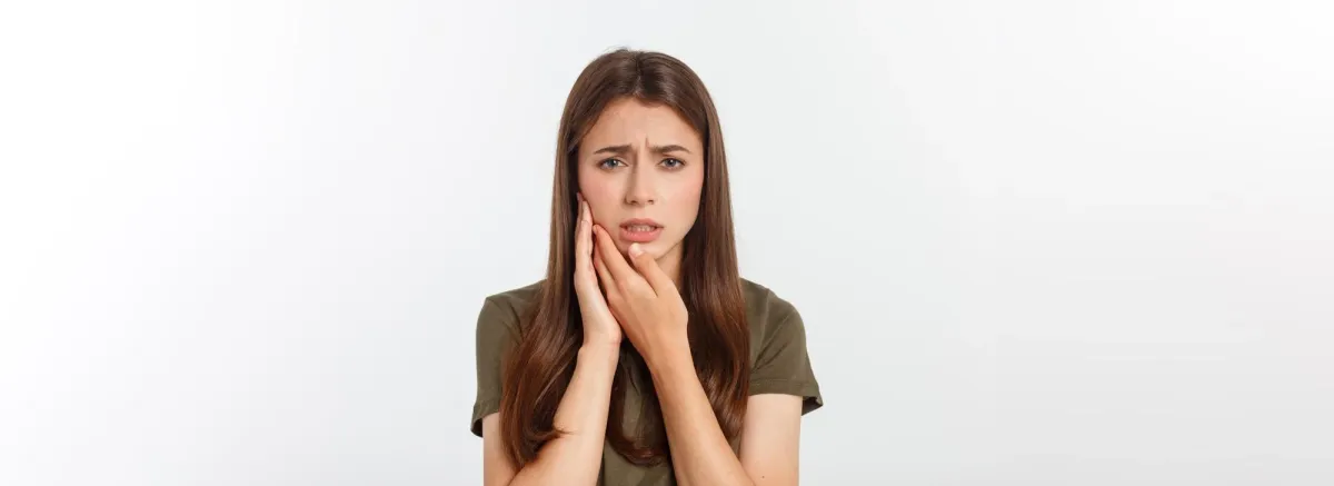 Young woman holding her cheek with a worried expression, representing burn gums and oral discomfort.