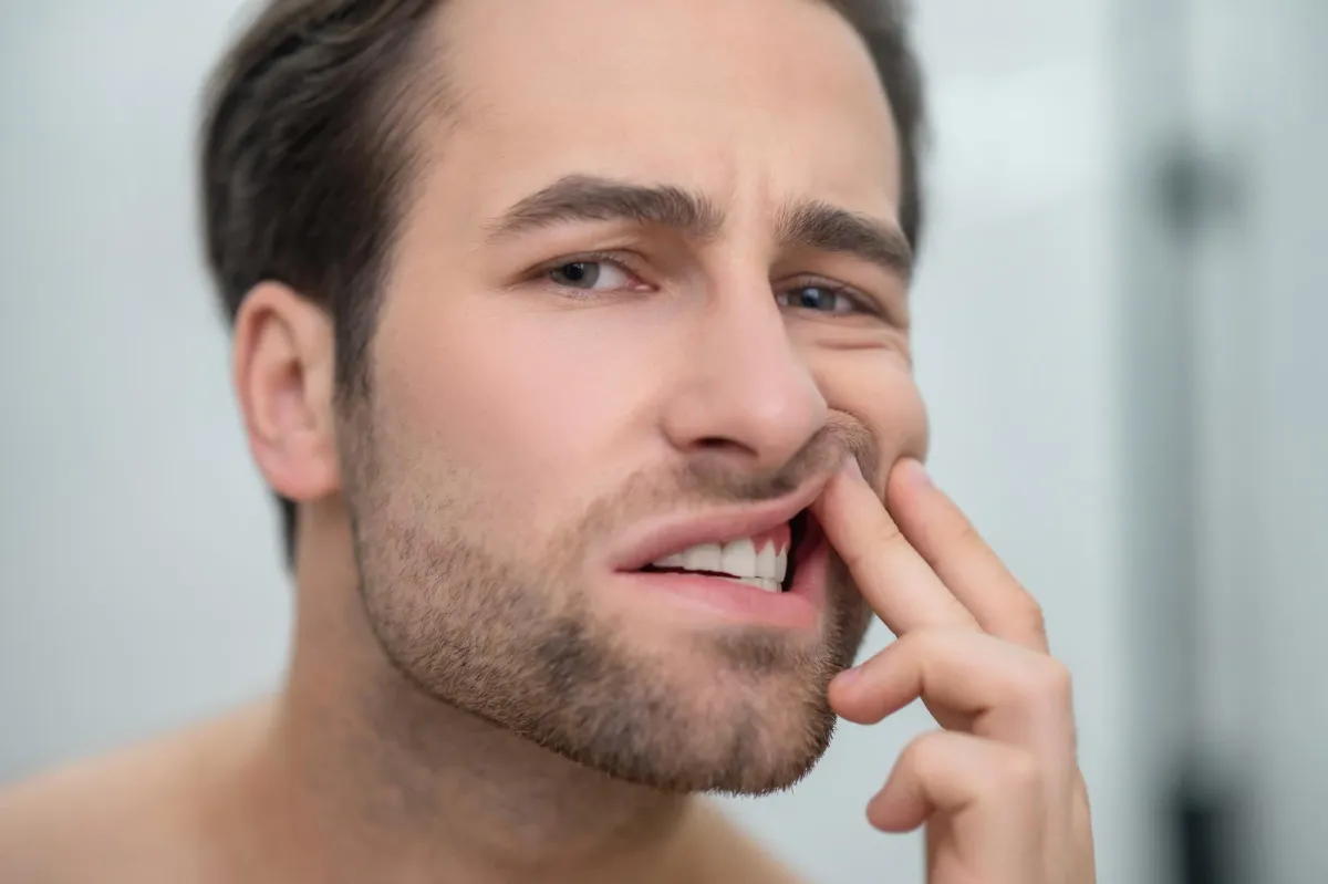 Close-up of a man gently pulling back his cheek and examining a red, irritated gum area near his teeth, showing signs of gum inflammation and oral discomfort.