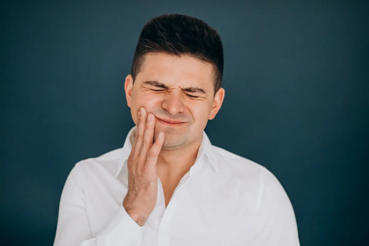 Man holding his cheek due to dental discomfort, representing symptoms of gum recession such as tooth sensitivity and gum pain.