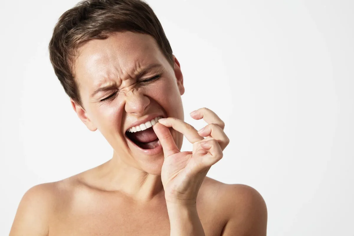 Featured image of a person experiencing gum discomfort and irritation, representing potential symptoms associated with White Spots on Gums
