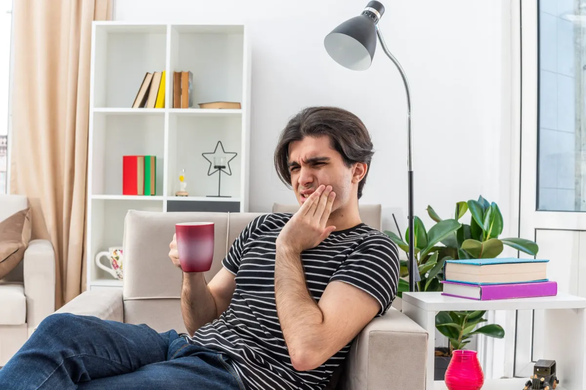 Person experiencing gums swollen and painful symptoms while drinking a hot beverage and holding their cheek in discomfort.