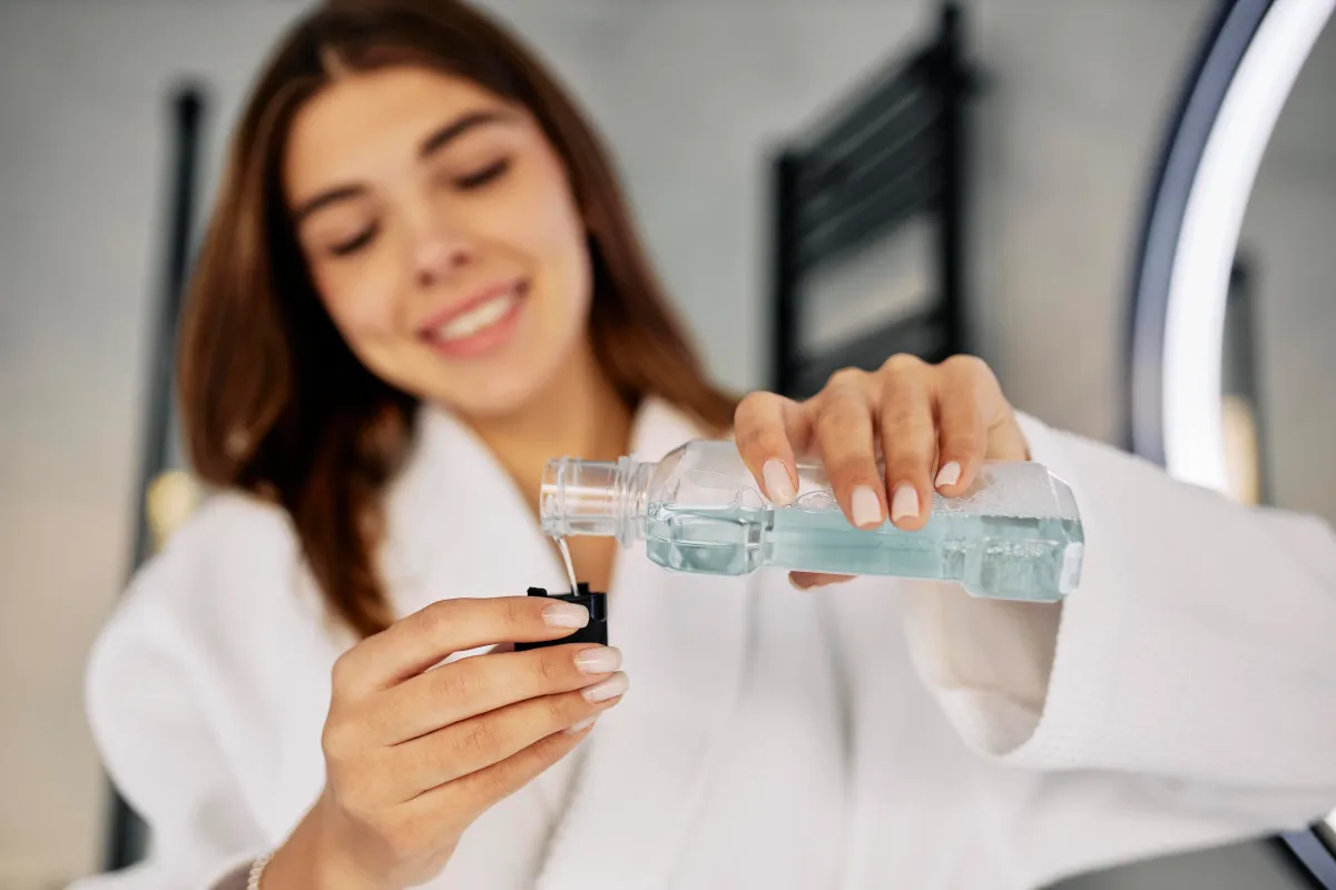 Woman pouring Antimicrobial Mouthwash into a cap before use as part of a daily oral hygiene and gum care routine.